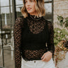 Front view of model wearing the Abby Black Lace Long Sleeve Top that has black sheer fabric, monochrome lace floral pattern, lettuce hem details, a high neck and long sleeves.