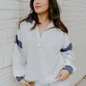 front view of model wearing the Rylan Grey & Navy Color Block Sweatshirt that has navy blue and heather grey knit fabric, color block striped pattern, raw hems, v-neck with collar, and long sleeves with cuffs.