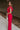 Full body side view of model wearing the Giana Hot Pink Wide Leg Ruffle Jumpsuit that has hot pink knit fabric, pockets, a ruffle details, a v-neck, a back zipper, and flare pant legs.