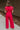 Full body back view of model wearing the Giana Hot Pink Wide Leg Ruffle Jumpsuit that has hot pink knit fabric, pockets, a ruffle details, a v-neck, a back zipper, and flare pant legs.