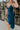 Close side view of mode wearing the Valerie Teal Sleeveless Ruffle Midi Dress that has teal knit fabric, a ruffle hem, a front slit, a v neck, spaghetti straps, and a back zipper with a hook closure.