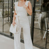 Full body view of model wearing the Clara Cream Ruffle Sleeveless Jumpsuit which features cream knit fabric, two slit pockets, waist tie closure with belt loops, square neckline, ruffle straps, sleeveless and monochrome back zipper with hook closure.