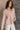 Side view of model wearing the Ada Dusty Rose Long Sleeve Top which features dusty mauve pink knit fabric, slight slits on each side, distressed details, a front left chest pocket, a v-neckline with collar, dropped shoulders, and long sleeves with cuffs.