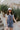 Front view of model wearing The Marina Washed Denim Romper features medium wash denim fabric, two front pockets, two back pockets, belt loops with a drawstring tie, one front chest pocket, a halter neckline, adjustable tie straps, a side zipper closure an