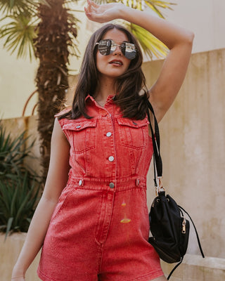 front image of modeal wearing The Emily Washed Red Denim Sleeveless Romper features washed red denim fabric, two front pockets, silver button details, button-up front, two front chest buttoned pockets, two back pockets, a collared neckline and a sleeveles
