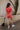 back full body image of modeal wearing The Emily Washed Red Denim Sleeveless Romper features washed red denim fabric, two front pockets, silver button details, button-up front, two front chest buttoned pockets, two back pockets, a collared neckline and a