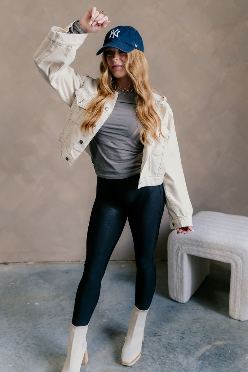 Full body view of model wearing the Kennedy Cream Button-Up Hoodie Jacket which features oatmeal color cotton fabric, a cropped waist, star detail buttons, two front buttoned chest pockets, dark brown stitch detailing, a hood, and long flare sleeves with 