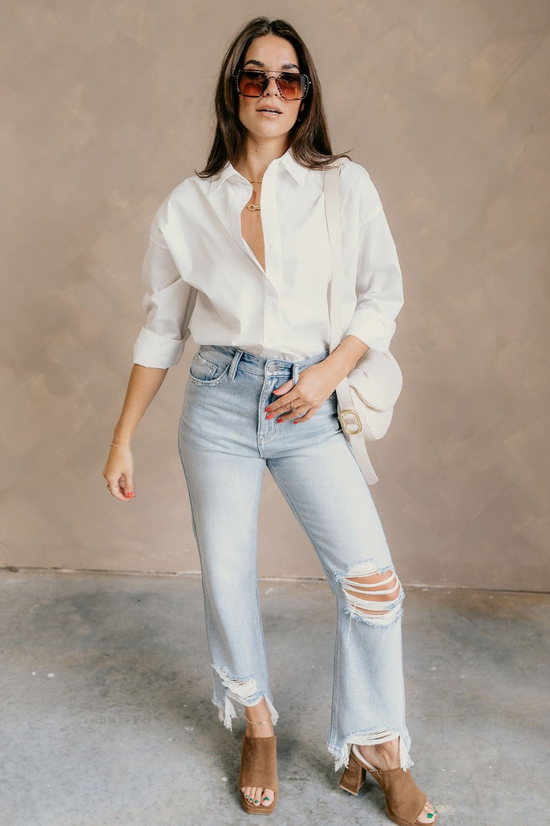 Full body view of model wearing the Gia White Button-Up Collared Long Sleeve Top which features white cotton fabric, monochromatic buttons, a collared neckline, and long sleeves with buttoned cuffs.