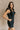 Front side view of model wearing the Avril Black Denim Ruffle Sleeveless Romper which features black washed denim fabric, pockets on each side, a front zip up, an elastic waistband, a square neckline, and ruffle straps.