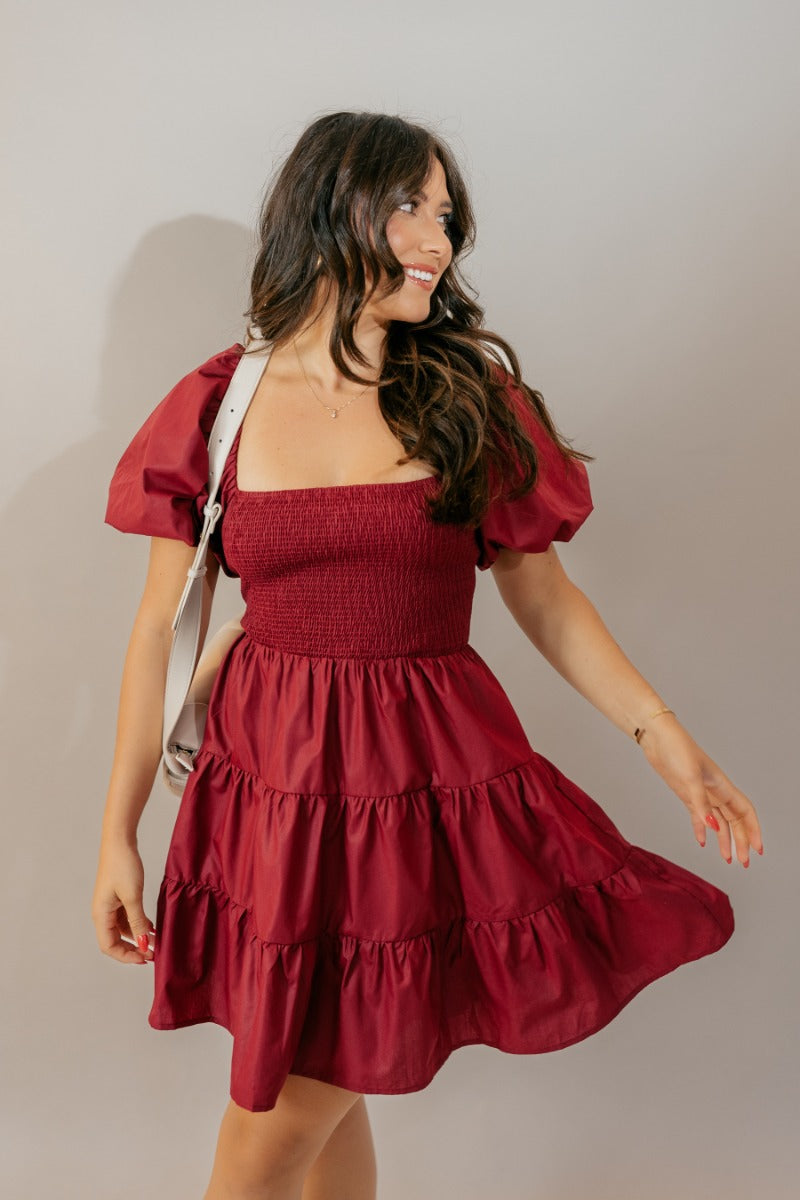 front view of model wearing the Willow Burgundy Puff Sleeve Dress that has burgundy fabric, mini length, a tiered skirt, smocked chest, a square neck and short puff sleeves