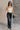 Full body front view of model wearing the Ceros: Florence Wide Leg Jeans that have black denim, a zipper and button closure, belt loops, high-rise waist, pockets, and wide cropped legs with distressed hems