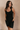 Front side view of model wearing the Amara Black Athletic Onesie Bodysuit that has black atheisure fabric, side pockets, built-in-padding, monochrome stitching, and thick straps. Sweater is draped on model's shoulders.