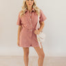 Full body front view of model wearing the Sadie Pink Knit Short Sleeve Romper that has washed pink knit fabric, pockets, a front zipper, a collar, belt loops, an elastic waistband, and short sleeves.