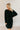 front view of model wearing the Sara Black Long Sleeve T-shirt Dress that has black cotton fabric, mini length, slits on each side, a round neckline, dropped shoulders, and long sleeves.