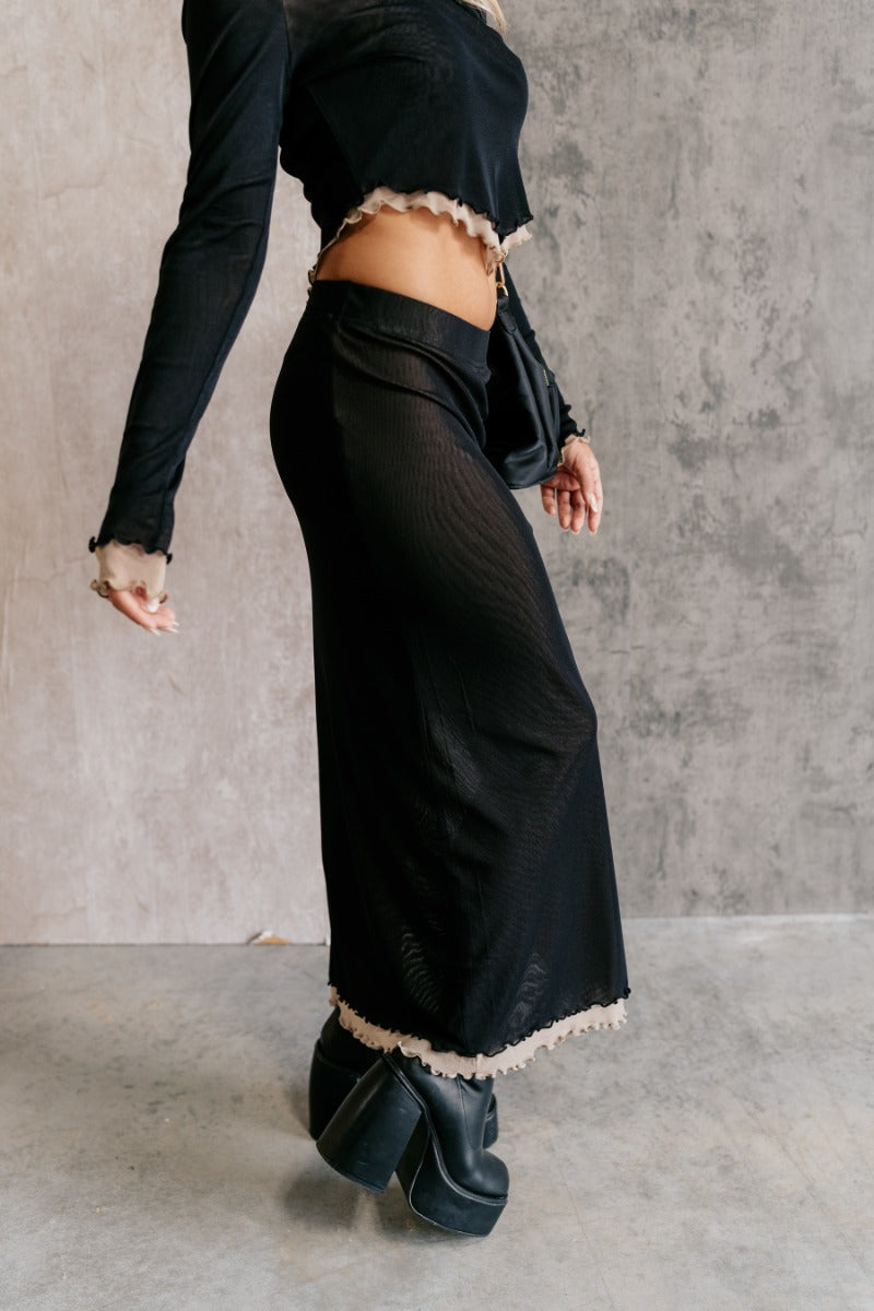 Side view of model wearing the Kylie Black & Taupe Mesh Midi Skirt that has black mesh fabric, taupe mesh lining, an elastic waist, a slit on the side, and lettuce hem details.