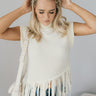 Front view of model wearing the Brielle Cream Fringe Hem Sleeveless Knit Sweater which features cream knit fabric, a slanted hem with fringe details, a high neckline and a sleeveless design.