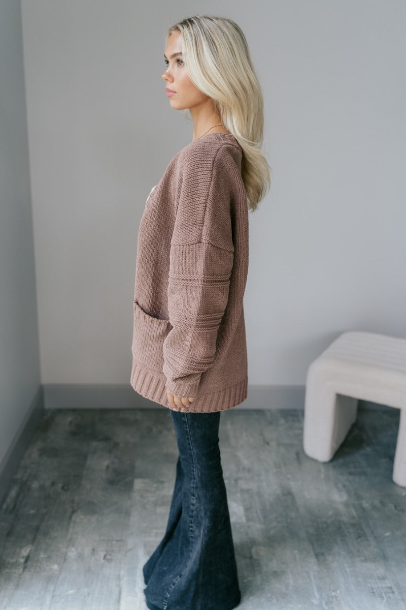 Full body side view of model wearing the Adaline Mocha Open Front Cardigan that has brown knit fabric, two front pockets, a front opening with no closure, dropped shoulders and long puff sleeves with cuffs.