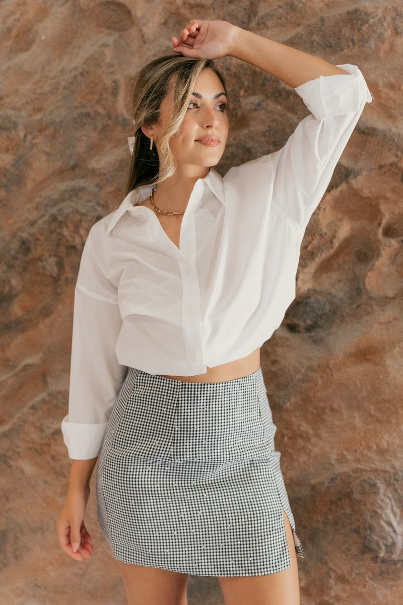 front view of model wearing the Everly Gingham Rhinestone Mini Skirt that has a black and white gingham design with rhinestones, a slit on the side, and a back white zipper with a hook closure.
