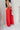 Full body side view of model wearing the Scarlett Red Wide Leg Pants which features red lightweight fabric, two front pockets, a front zipper with a hook closure, belt loops and wide legs.