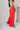 Full body side view of model wearing the Scarlett Red Wide Leg Pants which features red lightweight fabric, two front pockets, a front zipper with a hook closure, belt loops and wide legs.
