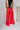 Full body back view of model wearing the Scarlett Red Wide Leg Pants which features red lightweight fabric, two front pockets, a front zipper with a hook closure, belt loops and wide legs.