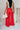 Full body back view of model wearing the Scarlett Red Wide Leg Pants which features red lightweight fabric, two front pockets, a front zipper with a hook closure, belt loops and wide legs.