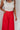 Close up view of model wearing the Scarlett Red Wide Leg Pants which features red lightweight fabric, two front pockets, a front zipper with a hook closure, belt loops and wide legs.
