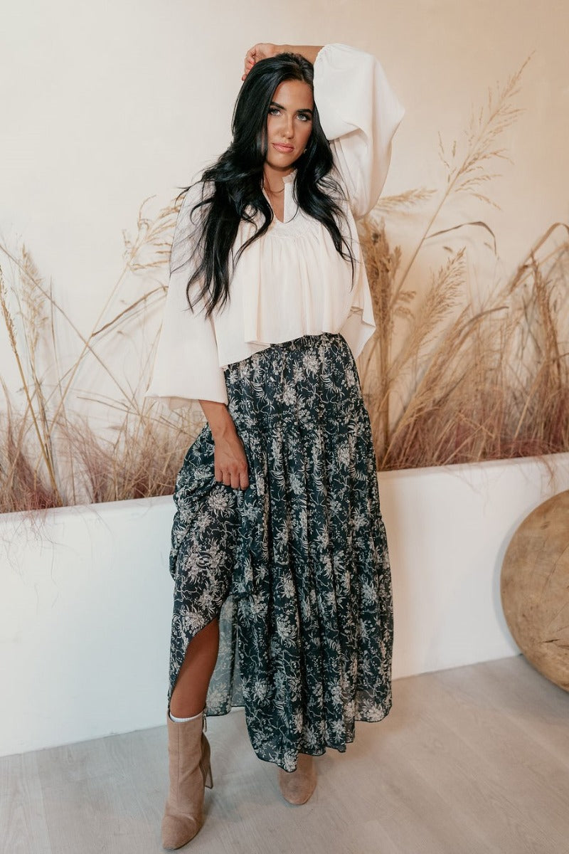 Full body front view of model wearing the Eleanor Charcoal & White Floral Maxi Skirt that hat grey semi-sheer fabric with white floral print, maxi length, tiered ruffles, thigh-length lining, and an elastic waist.