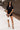 Full body front view of model wearing the Running The Show Denim Romper, which features black washed denim, a surplice neck that snaps with a collar, half-length sleeves, a front zipper, pockets, pleating on the legs, and a 3" inseam