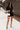 Full body front view of model wearing the Running The Show Denim Romper, which features black washed denim, a surplice neck that snaps with a collar, half-length sleeves, a front zipper, pockets, pleating on the legs, and a 3" inseam