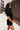 Side view of model wearing the Running The Show Denim Romper, which features black washed denim, a surplice neck that snaps with a collar, half-length sleeves, a front zipper, pockets, pleating on the legs, and a 3" inseam