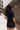Close-up back view of model wearing the Running The Show Denim Romper, which features black washed denim, a surplice neck that snaps with a collar, half-length sleeves, a front zipper, pockets, pleating on the legs, and a 3" inseam
