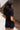 Close-up back view of model wearing the Running The Show Denim Romper, which features black washed denim, a surplice neck that snaps with a collar, half-length sleeves, a front zipper, pockets, pleating on the legs, and a 3" inseam