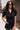 Front view of model wearing the Running The Show Denim Romper, which features black washed denim, a surplice neck that snaps with a collar, half-length sleeves, a front zipper, pockets, pleating on the legs, and a 3" inseam
