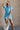 Full body view of model wearing the Delilah Washed Sky Blue Short Sleeve Romper which features washed light blue tencel fabric, two front slit pockets, an elastic waistband with a drawstring tie, a right front chest pocket, tortoise button closures, a col