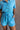 Close up view of model wearing the Delilah Washed Sky Blue Short Sleeve Romper which features washed light blue tencel fabric, two front slit pockets, an elastic waistband with a drawstring tie, a right front chest pocket, tortoise button closures, a coll