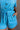 Close up view of model wearing the Delilah Washed Sky Blue Short Sleeve Romper which features washed light blue tencel fabric, two front slit pockets, an elastic waistband with a drawstring tie, a right front chest pocket, tortoise button closures, a coll