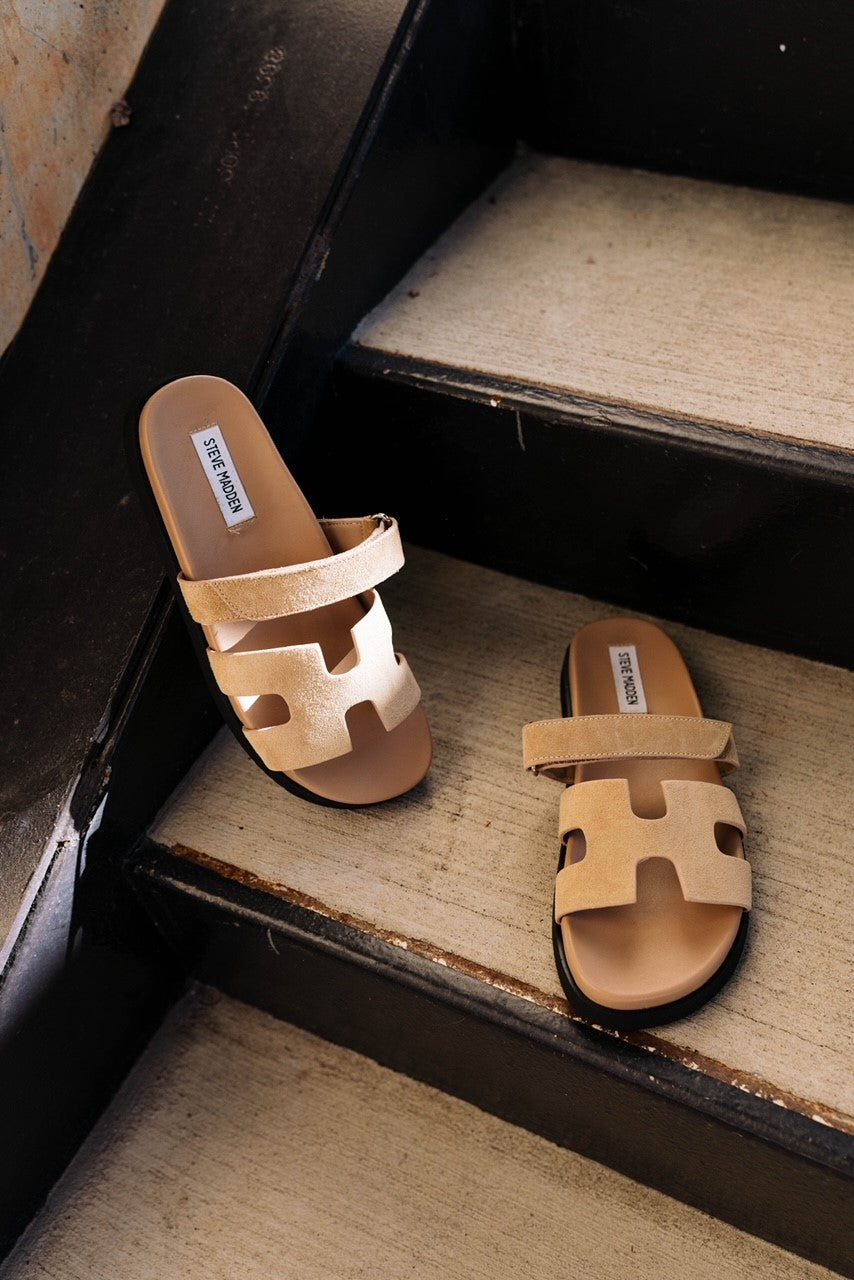 Ariel view of the Mayven Sandal in Taupe Suede which features taupe suede fabric, adjustable hook and velcro closure strap, "h" shaped strap, round toe, slide one style and black sole.