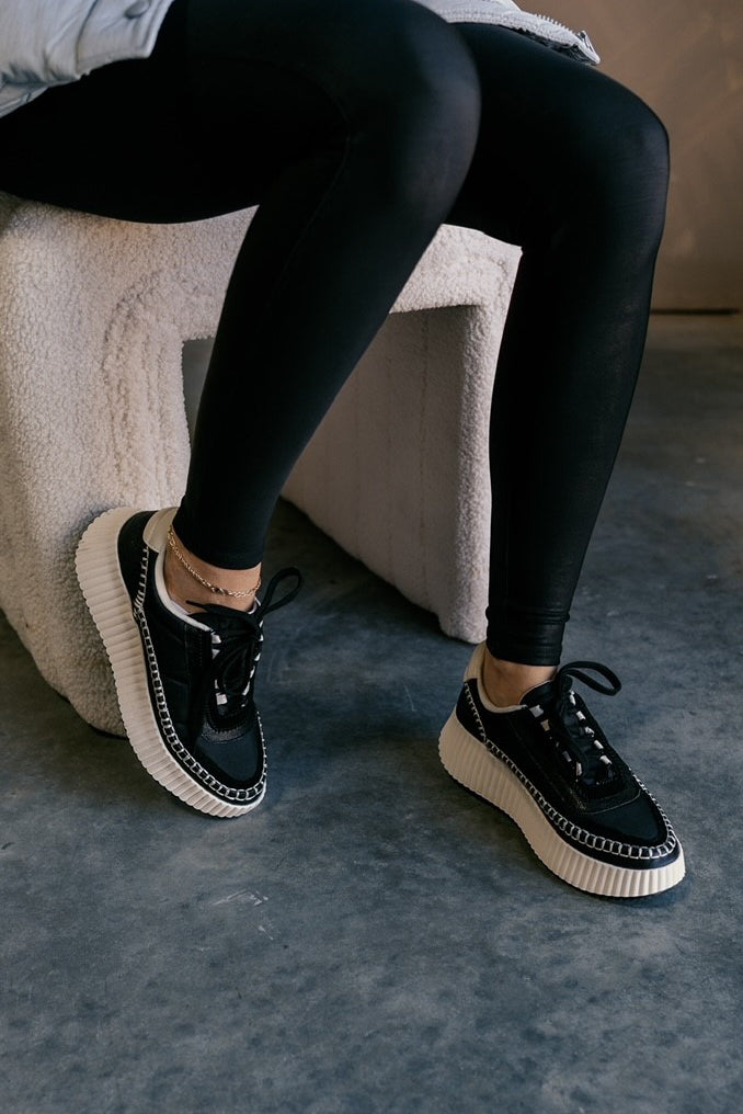 Right front angle view of female model wearing the Dolen Nylon Sneaker in Black Nylon which features black leather and nylon upper fabric, off white rubber platform sole, black lace up closure and off white stitch details.