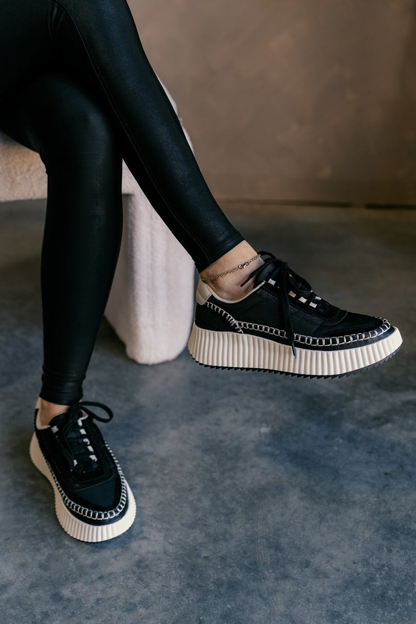 Right front angle view of female model wearing the Dolen Nylon Sneaker in Black Nylon which features black leather and nylon upper fabric, off white rubber platform sole, black lace up closure and off white stitch details.