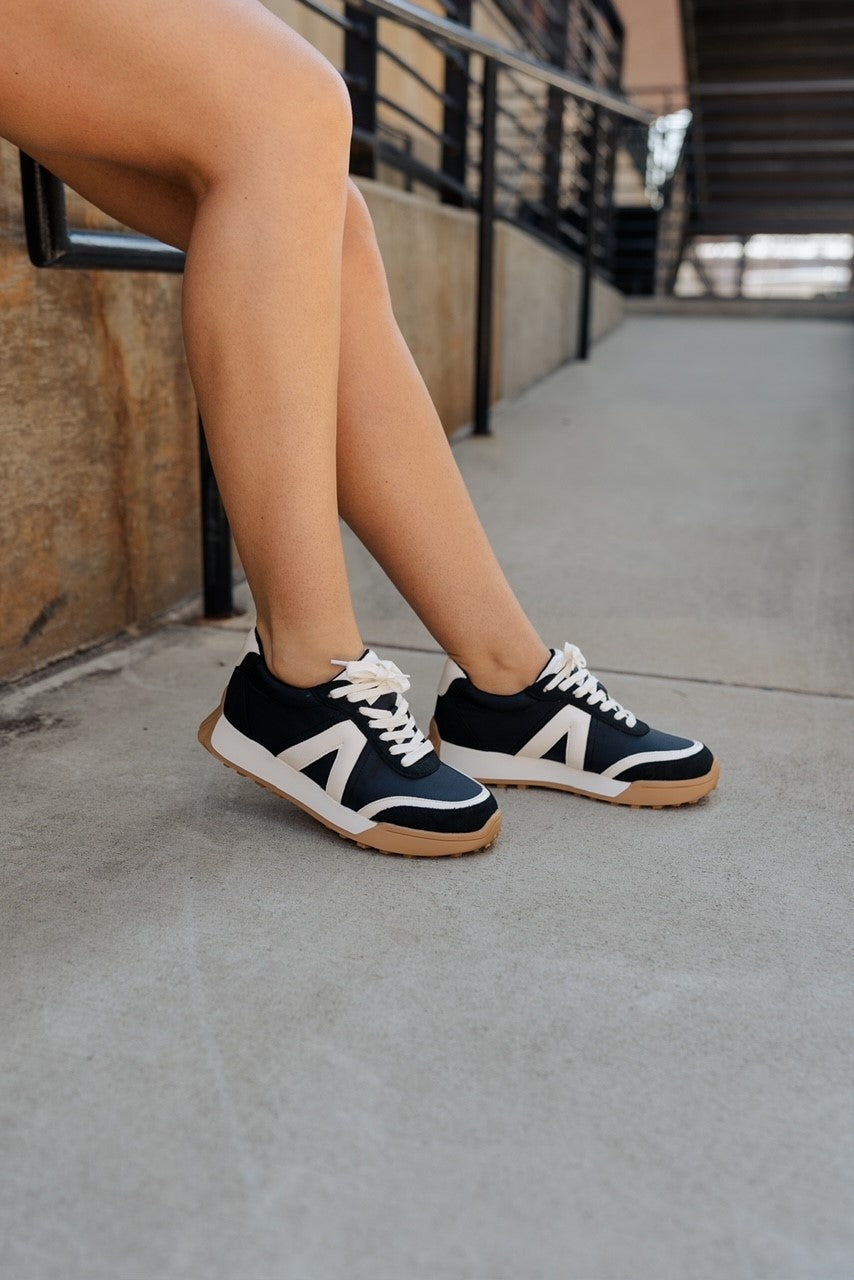 Side view of model wearing the Town Sneaker which features black and white fabric, white lace up closure, contrast details, suede accents and have a gripped brown 1.4-inch outsole.