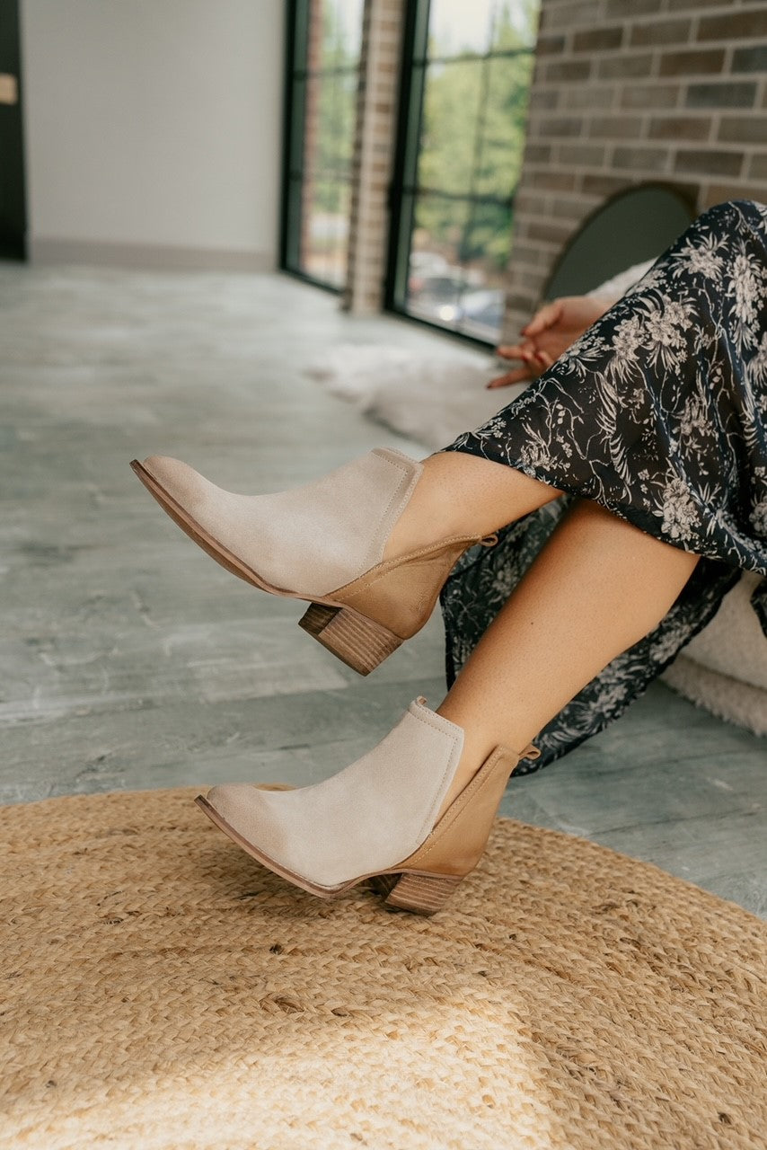 Frontal side view of female model wearing the Stop By Bootie which features brown and grey suede and leather fabric, color-block design, slits on both side, block heel, almond-toe shape and pull on tabs