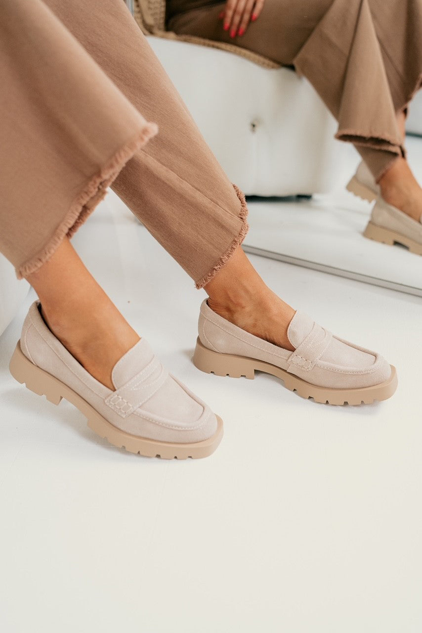 Right front angle view of the female model wearing the Elias Flat in Dune Suede which features tan suede upper fabric, monochrome rubber sole, slide-on style and slight square toe design.