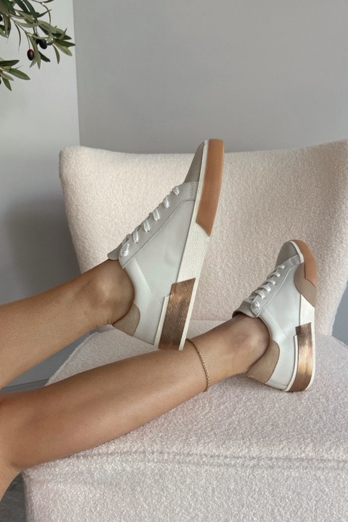 Side view of female model wearing the Zina Sneaker in White Tan Leather which features white, tan, and metallic leather fabric, natural suede fabric, round toe and lace up closure.