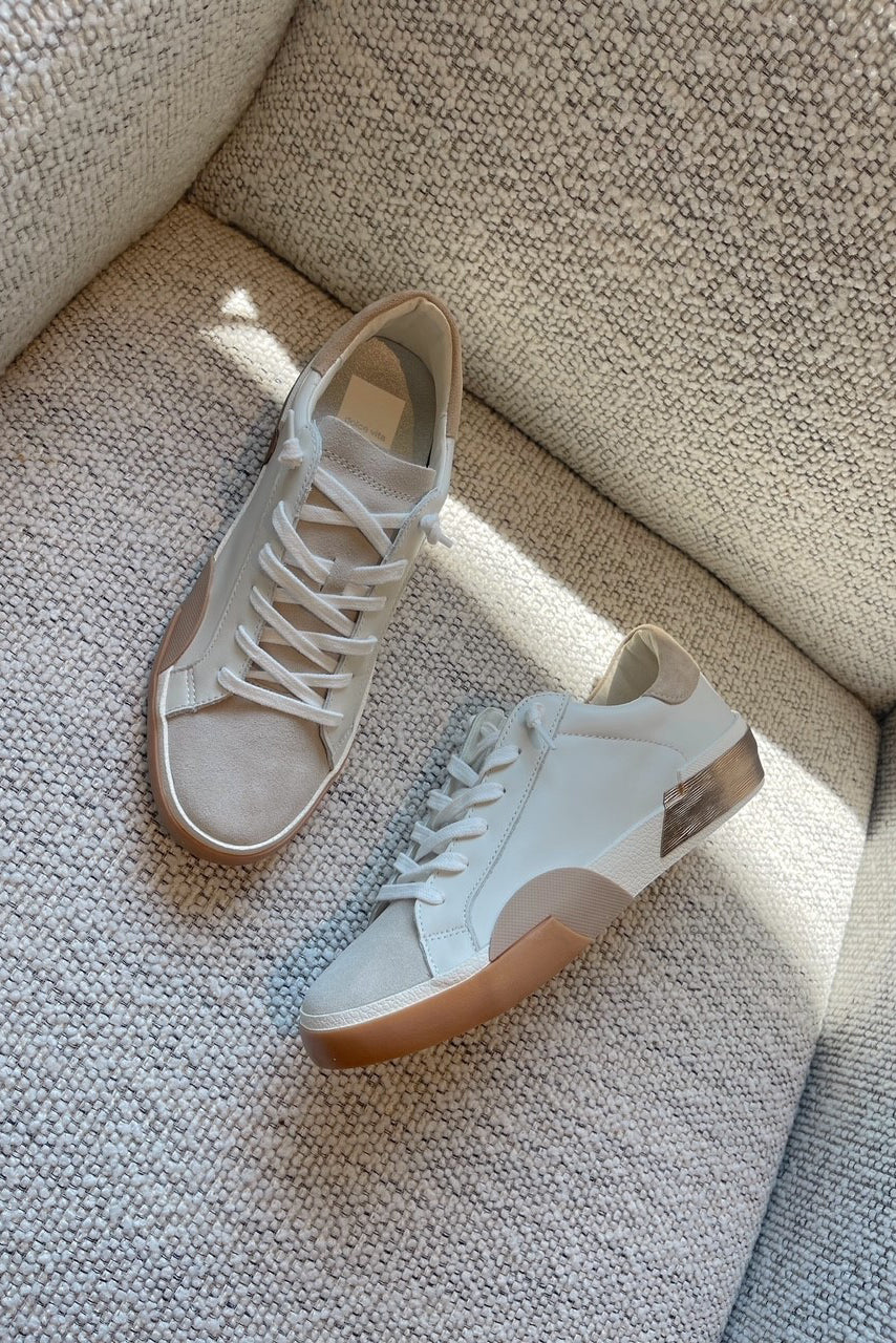 Flat lay view of female model wearing the Zina Sneaker in White Tan Leather which features white, tan, and metallic leather fabric, natural suede fabric, round toe and lace up closure.