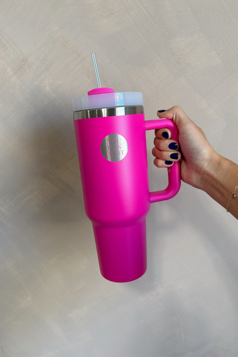 Hand is holding the You Can Do It Tumbler which is a hot pink 40 oz  tumbler featuring a silver "You Can Do It" graphic. Front view