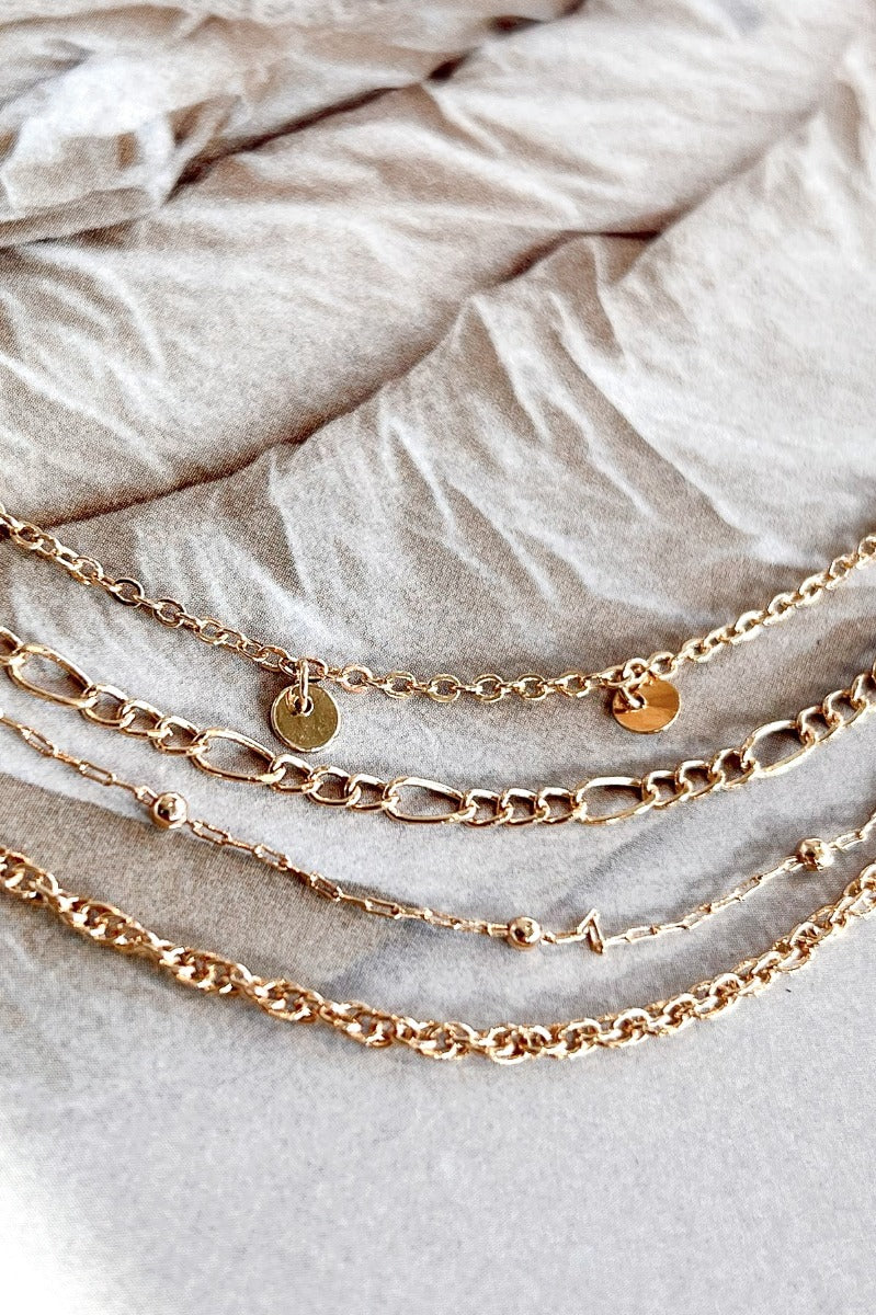 Close-up image of the Once Upon A Time Necklace, that  features four varied gold chains with small gold beads and circle charms.