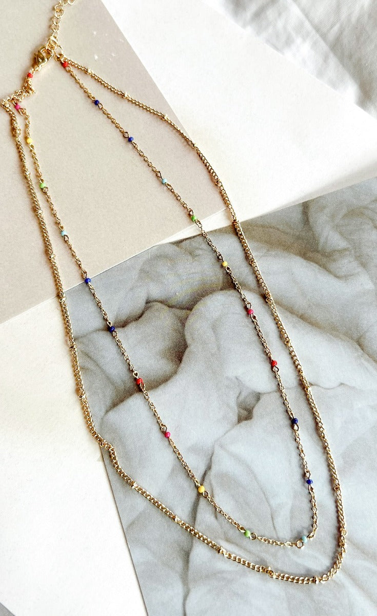 Aerial image of the Brighten Your Day Necklace, that features double gold chains and multi-colored beads.