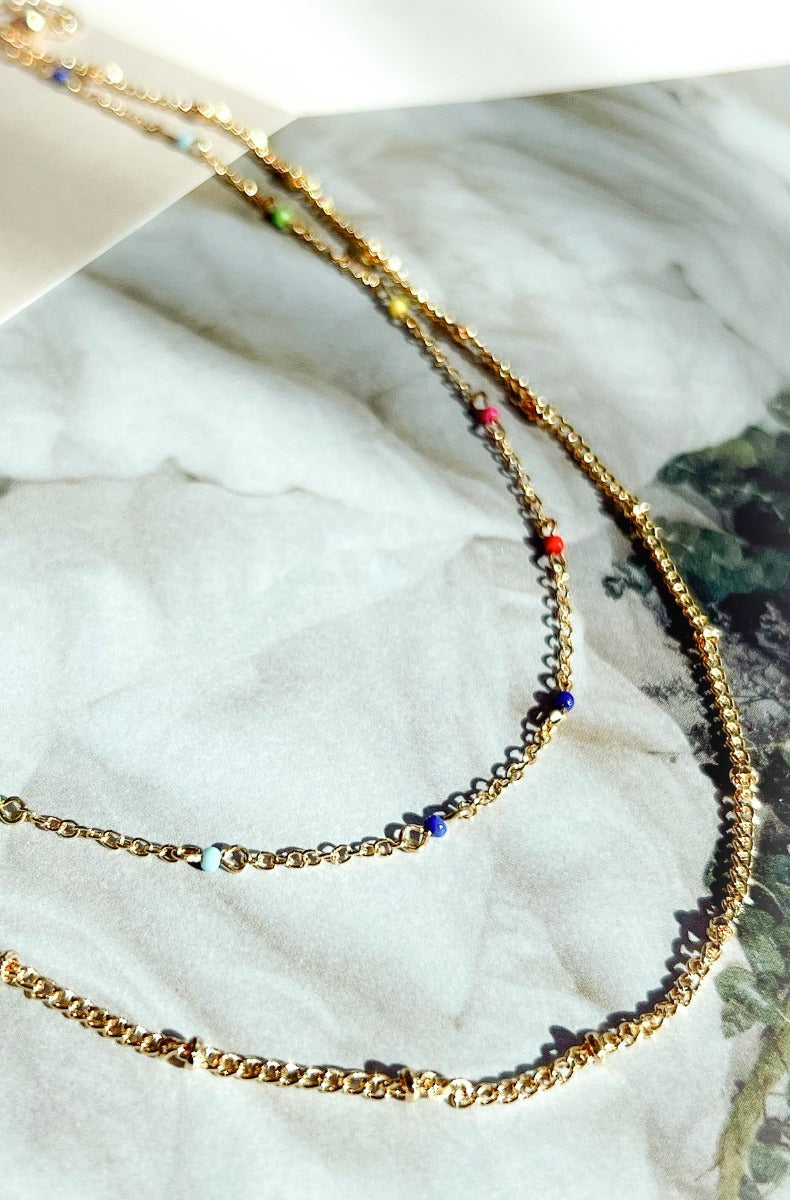 Close up image of the Brighten Your Day Necklace, that features double gold chains and multi-colored beads.