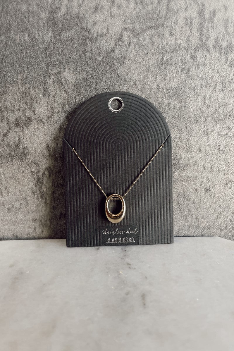Front view of the Cecilia Gold Oval Necklace that has a gold link chain with an open oval pendant and an adjustable clasp closure, pictured on a black necklace card.